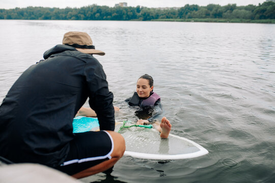 Young woman learns how to stand up on wakesurf board under guidance of coach.