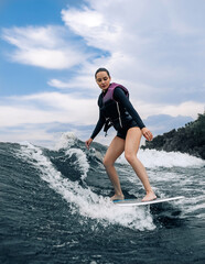 Young woman wakesurfing on wave from a motorboat.