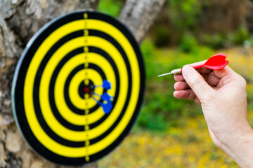 Hand with red arrow darts to throw on dartboard hanging at the tree with sunlight  that sport...