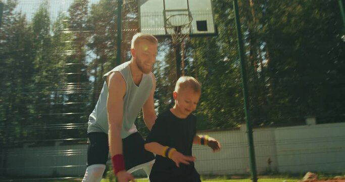 American athletes trainer and little boy kid playing basketball outdoors training on basketball court