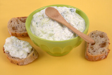 Bol de tzatziki avec une cuillère en bois et des tartines de pain en gros plan sur fond jaune