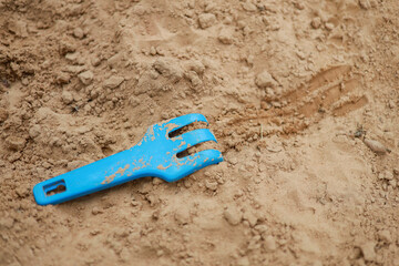 Fototapeta na wymiar Small kids blue plastic rake with sand marks.