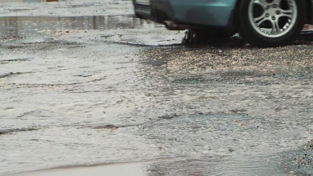 Puddles and pits on the asphalt, road infrastructure damaged after rain. Cars are moving slowly along the road with potholes. Asphalt in violation of technology. Taxpayer money is wasted. UHD 4K.