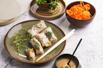 Several spring rolls with chicken, carrot and bamboo sprouts in rice paper on green plate, sesame sauce and coriander on concrete surface