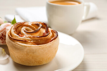 Freshly baked apple rose, cup of coffee and beautiful flowers on white wooden table