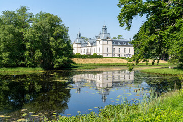 Fototapeta na wymiar picturesque Kronovall Castle and gardens reflected in a pond in the foreground on a summer dday under a blue sky