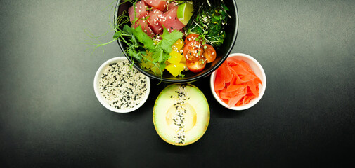 Poke salad with tuna in a bowl. Ingredients fresh tuna, cherry tomatoes, marinated seaweed, rice, takuan, Ponzu sauce, Teriyaki sauce, nori, sesame seeds, lime, cilantro. Asian seafood salad concept.