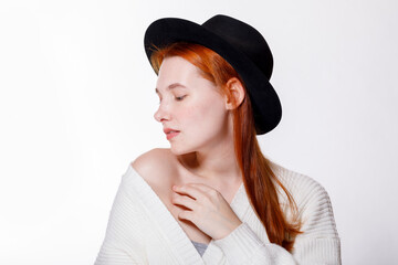 A sensual portrait of a young attractive woman with red hair and a black hat on a white background.