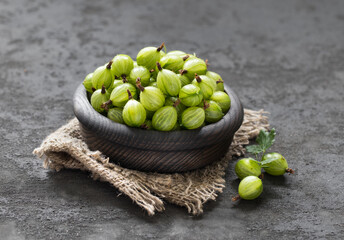 Fresh gooseberries in a wooden bowl on a linen napkin on a dark gray background