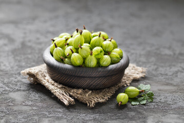 Fresh gooseberries in a wooden bowl on a linen napkin on a dark gray background