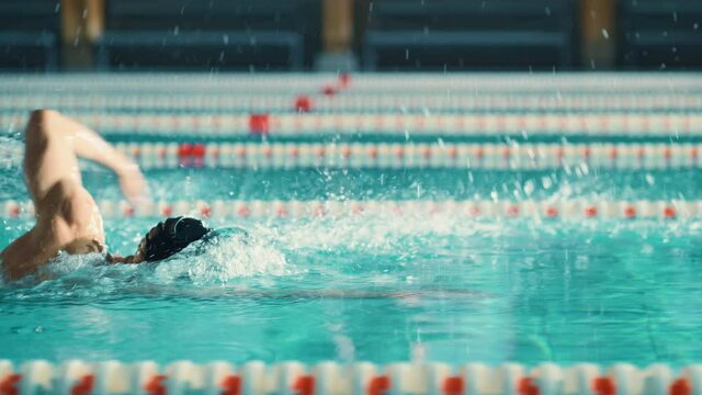 Successful Male Swimmer Racing, Swimming in Swimming Pool. Professional Athlete Determined to Win Championship Freestyl Crawl Stroke Colorful Cinematic Shot. Side View Tracking Slow Motion