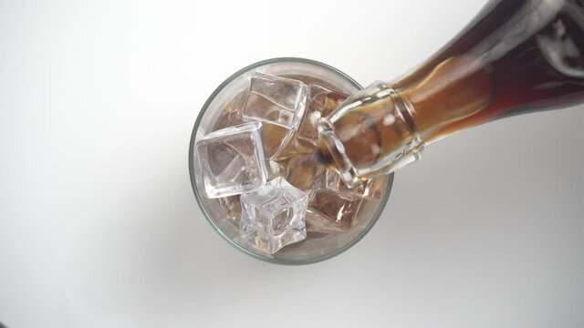 Vertiendo refresco de cola en un vaso con hielos, vista desde arriba
