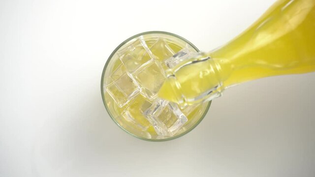 Vertiendo refresco de naranja en un vaso con hielos, vista desde arriba