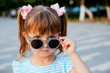 A little girl is standing in sunglasses. Protection from sunlight. Entertainment and pampering of the child.