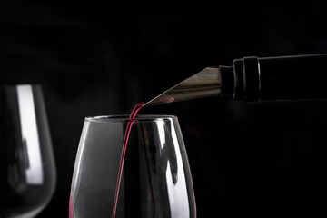 close-up of wine being poured into a glass with dark background.