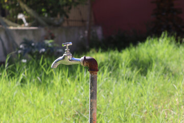 Selective focus of a shiny faucet with an old and rustic pipe against a blurry grass background