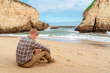 Rear view of a blonde man in a shirt on the beach of Shark Fin Bay on the California coast. Beautiful panoramic landscape