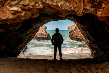 Fototapeta premium The silhouette of a man in a dark cave with a view of the raging ocean and rocks