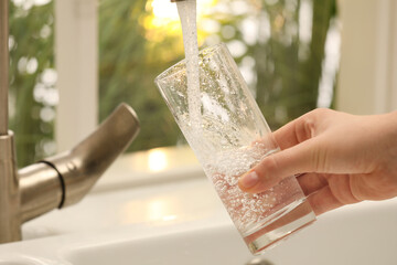 Woman filling glass with water from tap at home, closeup