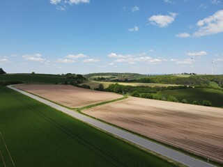 Aerial view of road between green and brown agriculture fields in the landscape with blue sky 