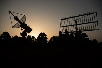 Space radar antenna on sunset. Silhouettes of satellite dishes or radio antennas against night sky....