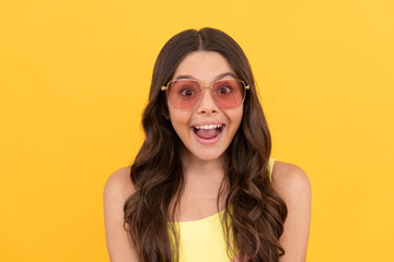 amazed teen girl in summer glasses has curly hair on yellow background, amazement and surprise