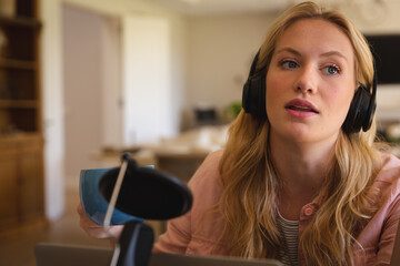 Caucasian woman wearing headphones and using microphone, talking during podcast