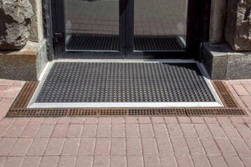 entrance to the store from a pedestrian sidewalk from a rubber doormat with storm drain lattice,...