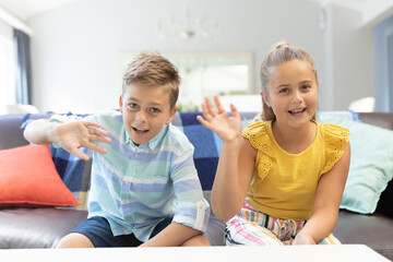 Caucasian brother and sister waving and smiling during video chat at home