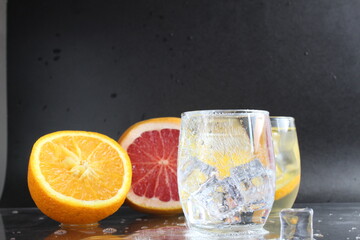 Cooking Lemonade Water in a glass of ice and fruit orange grapefruit on a black background. Summer drinks. A lemonade drink
