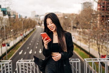 Long hair brunette Asian woman using mobile phone in the street