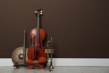 Set of different musical instruments near brown wall indoors, space for text - obrazy, fototapety, plakaty