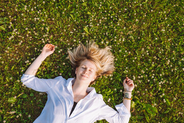Top view of a young woman lying on a meadow with blooming clover with closed eyes. Insects, allergies, spring mites
