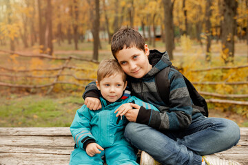 Fototapeta na wymiar Funny brothers who are smiling happily together. Two happy boys in the woods. Two brothers play outdoors in autumn, best friends. Little brother with brother sit at the outdoor. Fraternal relations