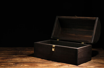 Empty treasure chest on wooden table against black background. Space for text