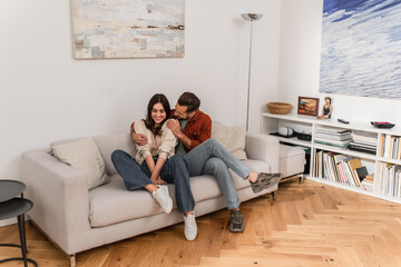 Smiling man embracing girlfriend on couch in living room