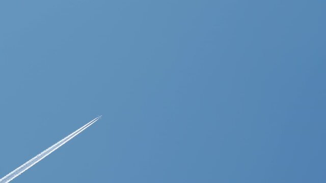 Passenger airplane at cruising altitude with contrail against blue sky