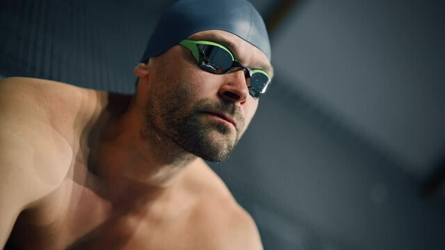 Handsome Professional Male Swimmer in Swimming Pool, Wearing Cap and Glasses, Looks Confidently at the Camera, Ready to Win the Championship. 
