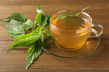 Glass cup of aromatic nettle tea and green leaves on wooden table, closeup