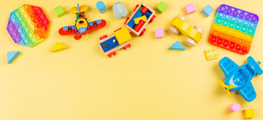 Baby kid toys banner background with wooden blocks, train, car, plane, pop it fidget toy on yellow background. Top view, flat lay, copy space