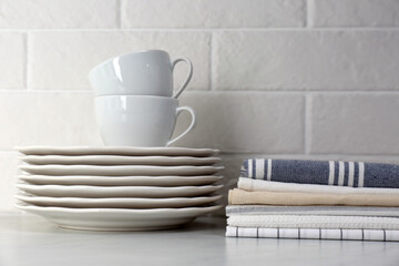 Fototapeta na wymiar Stack of soft kitchen towels and dishware on table near white brick wall