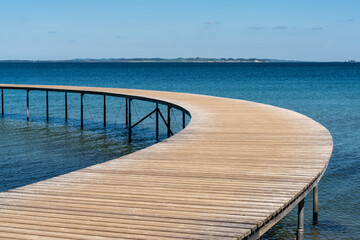 curved wooden boardwalk leads out into the blue ocean