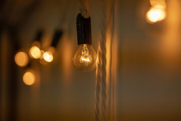 Round small bulb glowing with warm orange light hang on a white wall. Loft-style decor. The bulbs are connected to each other like a garland. Close-up, bokeh blurred background