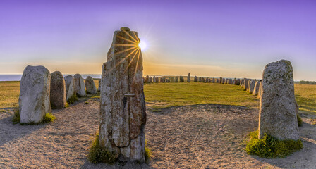 view of the prehistoric Ales Stenar ship setting on the southern coast of Sweden at sunset under a...