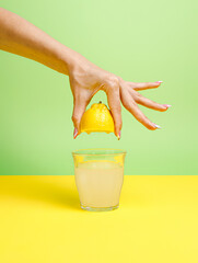 A woman's hand squeezing half of a lemon and making a glass of icy cold lemonade isolated on a...
