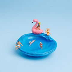 Seashell as a pool represent holiday season with swimmers and flamingo toy on pastel blue background. Tourism and leisure idea. Creative summer vacation concept.