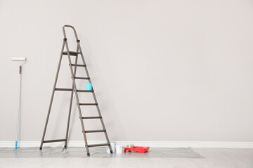 Decorator's tools and ladder near white wall indoors, space for text