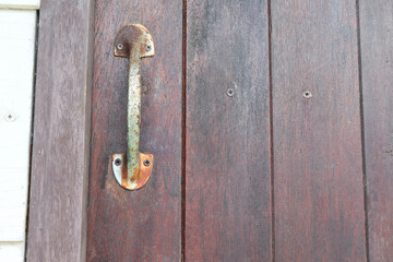 Old and rusty door handle on the wooden door is closing.