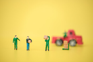 Group of miniature warehouse workers carrying goods box from semi truck on yellow background. logistics warehouse freight transportation concept. Use for banner or article website
