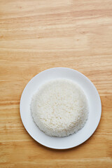 flat lay top view shot of streamed white Thai's jasmine rice in the white clean dish isolated put on the wooden plate dinner table closed to one conner of the photo with empty copy space for texts